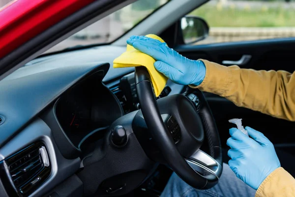 Vista parcial del hombre en guantes de látex usando antiséptico y trapo para la desinfección interior del coche durante la pandemia de coronavirus - foto de stock