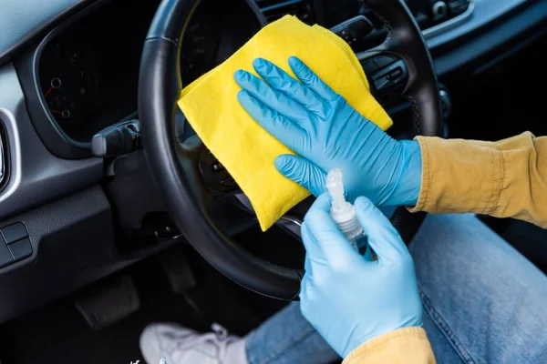 Cropped view of man in latex gloves using antiseptic and rag for cleaning car interior during coronavirus pandemic — Stock Photo