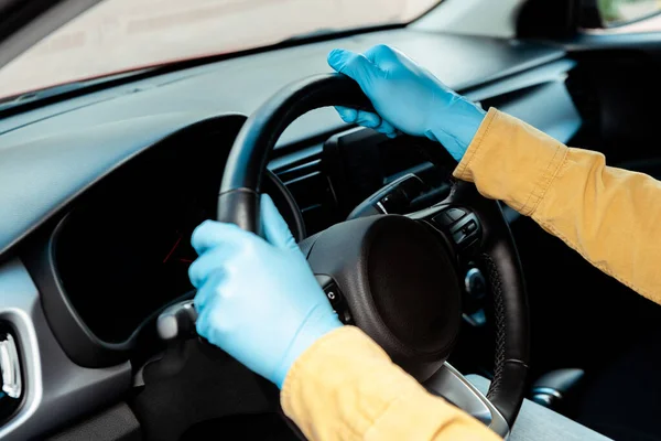 Ausgeschnittene Ansicht des Fahrers in Schutzhandschuhen, der das Lenkrad während der Covid-19-Pandemie hält — Stockfoto