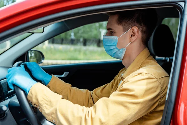 Driver in medical mask and protective gloves holding steering wheel in car during covid-19 pandemic — Stock Photo