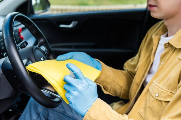 Обрезанный вид человека в латексных перчатках с использованием антисептика и тряпки для дезинфекции салона автомобиля во время пандемии ковида-19 — стоковое фото