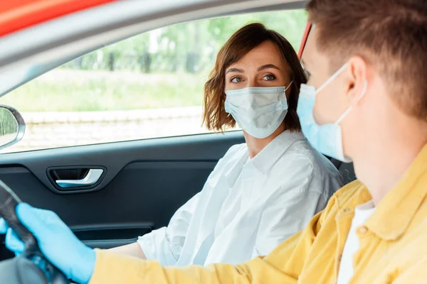 Homem e mulher em máscaras médicas e luvas de proteção sentados no carro durante a pandemia de covid-19 — Fotografia de Stock
