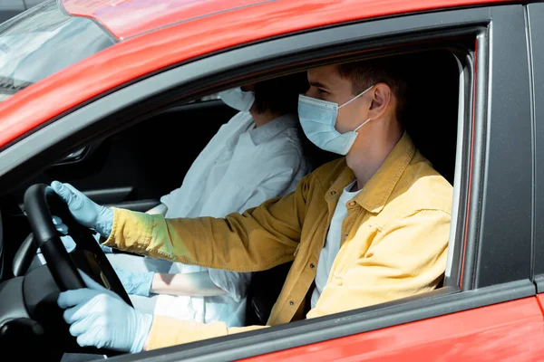 Мужчина и женщина в медицинских масках и защитных перчатках сидят в машине во время пандемии коронавируса — стоковое фото