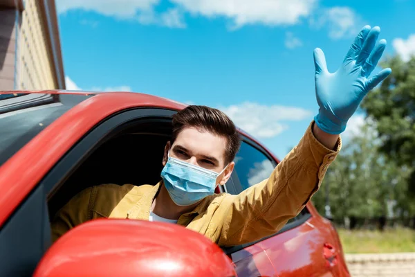 Man in medical mask and protective gloves waving and driving taxi during covid-19 pandemic — Stock Photo