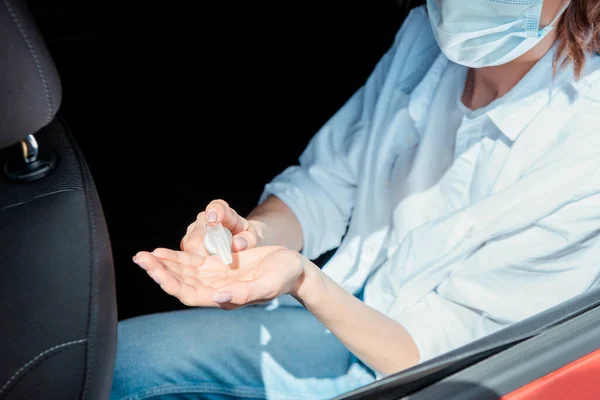 Cropped view of woman in medical mask using antiseptic in car during coronavirus pandemic — Stock Photo
