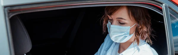 Mujer con máscara médica sentada en el coche durante la pandemia de covid-19 - foto de stock