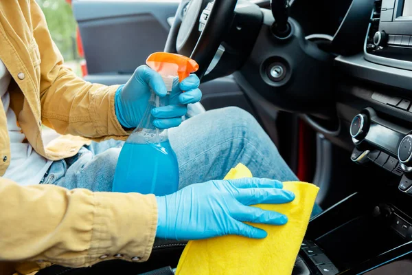Visão parcial do homem em luvas de látex usando spray anti-séptico e pano para limpar o interior do carro durante a pandemia de covid-19 — Fotografia de Stock