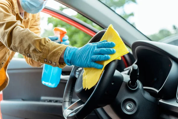 Cropped view of man in latex gloves and medical mask using antiseptic spray and rag for cleaning car interior during coronavirus pandemic — Stock Photo
