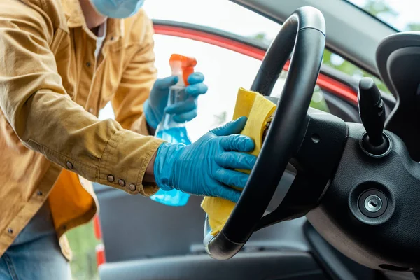 Cropped view of young man in latex gloves using antiseptic spray and rag for cleaning car interior during coronavirus pandemic — Stock Photo