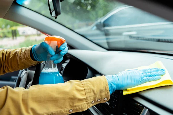 Visão cortada do homem em luvas de látex usando spray anti-séptico e pano para limpar o interior do carro durante a pandemia de coronavírus — Fotografia de Stock