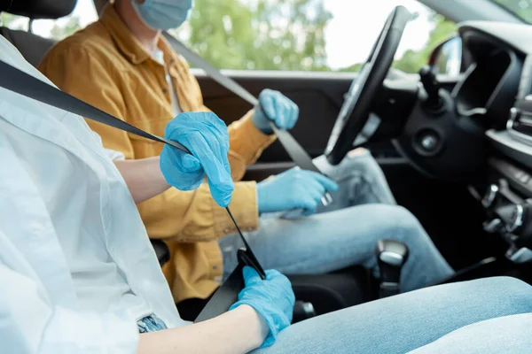 Vista recortada del hombre y la mujer en guantes de protección abrocharse los cinturones de seguridad en el coche durante la pandemia de covid-19 - foto de stock