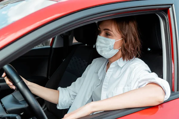 Mujer en máscara médica coche de conducción durante la pandemia covid-19 - foto de stock