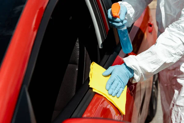 Cropped view of specialist in hazmat suit cleaning car with disinfectant spray and rag during covid-19 pandemic — Stock Photo