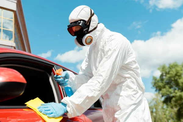 Specialist in hazmat suit and respirator cleaning car with antiseptic spray and rag during coronavirus pandemic — Stock Photo