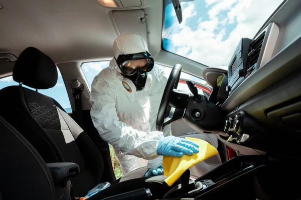 Specialist in hazmat suit and respirator cleaning car interior with rag on quarantine — Stock Photo