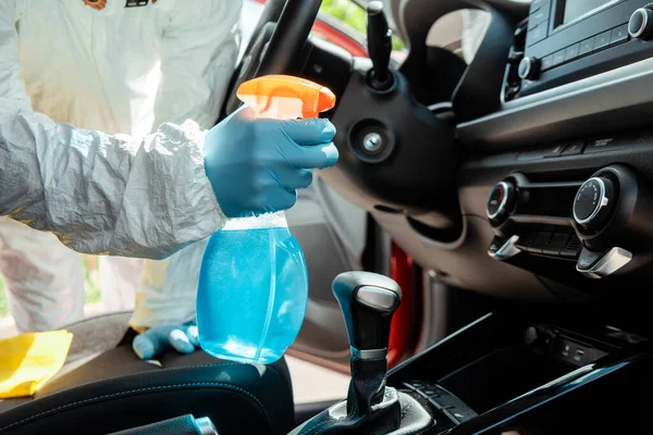 Vista recortada de especialista en traje de hazmat limpieza interior del coche con spray antiséptico durante la pandemia de coronavirus - foto de stock