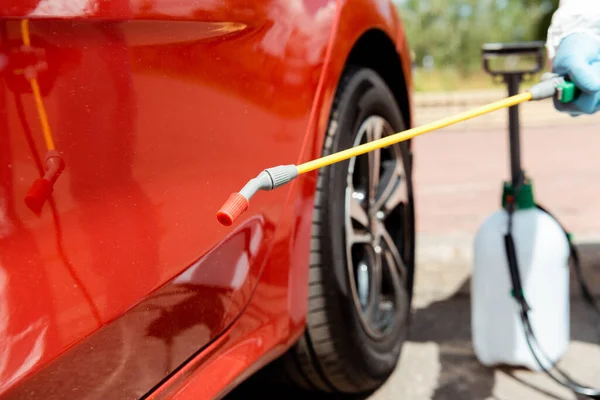 Vue recadrée du spécialiste en combinaison de protection voiture de nettoyage avec désinfectant pulvérisation pendant la pandémie covid-19 — Photo de stock