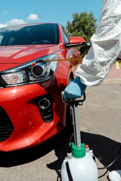 Vista recortada del trabajador en traje de hazmat coche de limpieza con desinfectante en bolsa de spray durante la pandemia de coronavirus - foto de stock