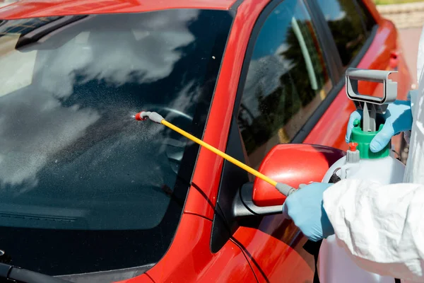 Vista recortada de protección en traje de hazmat coche de limpieza con desinfectante en bolsa de spray durante la pandemia de coronavirus - foto de stock