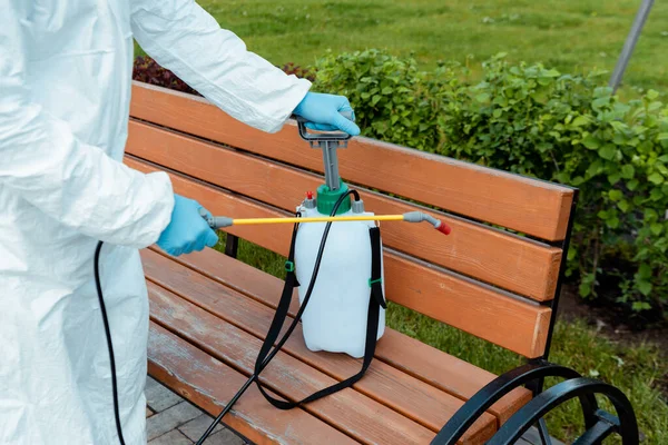 Vue recadrée du spécialiste en combinaison et respirateur désinfectant banc dans le parc pendant la pandémie de coronavirus — Photo de stock