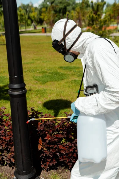 Professional specialist in hazmat suit and respirator disinfecting lamppost in park during coronavirus pandemic — Stock Photo