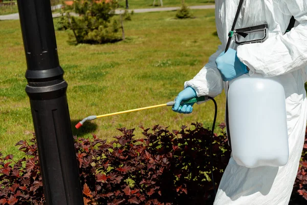 Vista recortada del especialista en traje de materiales peligrosos y respirador que desinfecta el poste de luz en el parque durante la pandemia de coronavirus - foto de stock