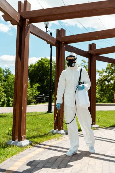 Spécialiste du nettoyage en uniforme et respirateur désinfecter la construction en bois dans le parc pendant la pandémie de coronavirus — Photo de stock