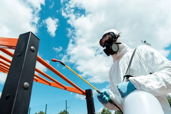 Especialista profesional en traje de felpudo y respirador desinfectando campo deportivo en parque durante pandemia de covid-19 - foto de stock