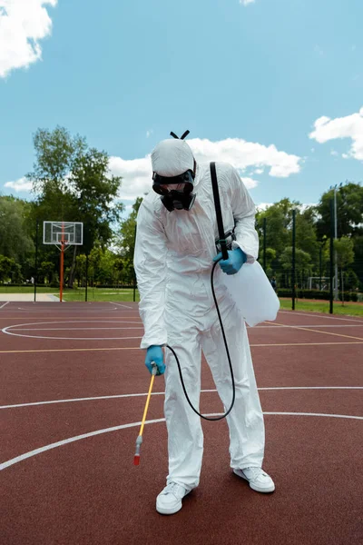 Worker in hazmat suit and respirator disinfecting basketball court in park during covid-19 pandemic — Stock Photo