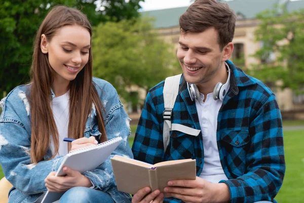 Happy girl writing in notebook near handsome student reading book — Stock Photo