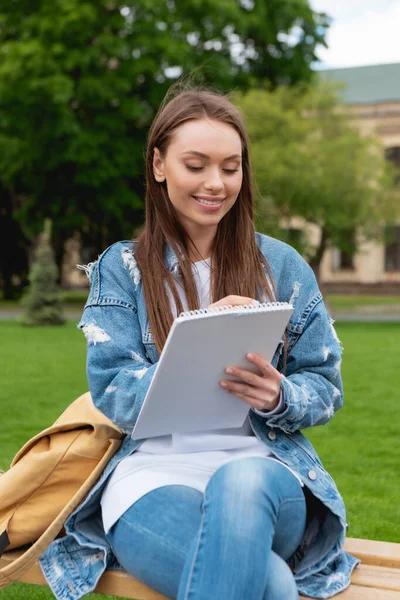 Jovem estudante feliz escrevendo em notebook no parque — Fotografia de Stock