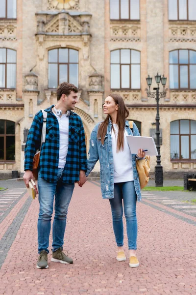 Cheerful students holding hands and looking at each other near university campus — Stock Photo