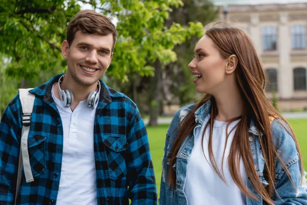 Fröhliches Mädchen schaut hübsche Studentin mit drahtlosen Kopfhörern an — Stockfoto