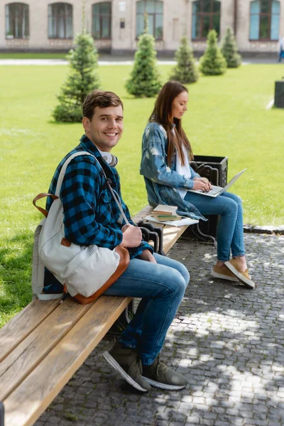 Selective focus of happy student smiling while girl using laptop near university campus, online study concept — Stock Photo