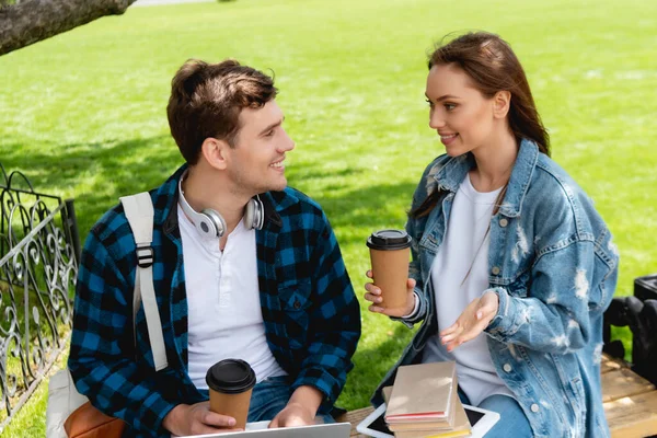 Feliz joven mujer mirando guapo estudiante mientras celebración de papel taza - foto de stock