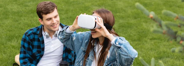 Tiro panorâmico de estudante alegre olhando para a menina feliz em fone de ouvido realidade virtual — Fotografia de Stock