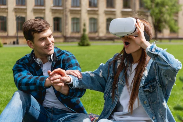 Étudiant joyeux tenant la main avec fille surprise dans un casque de réalité virtuelle — Photo de stock