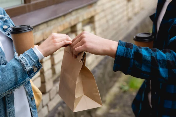 Vista ritagliata dello studente dando sacchetto di carta mentre tenendo tazza usa e getta — Foto stock