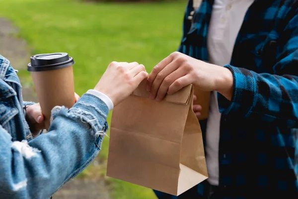 Recortado vista de estudiante dando bolsa de papel mientras niña sosteniendo taza desechable - foto de stock