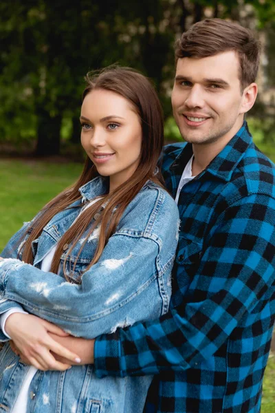 Feliz estudiante abrazando atractiva novia en chaqueta de mezclilla - foto de stock