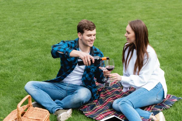 Uomo allegro versando vino rosso vicino fidanzata attraente, mentre avendo pic-nic — Foto stock