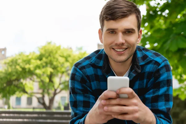 Estudiante feliz sonriendo mientras usa el teléfono inteligente - foto de stock