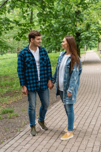 Alegre pareja de estudiantes tomados de la mano y mirándose en el parque - foto de stock