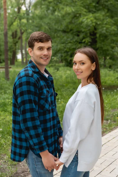 Freund und Freundin halten Händchen und blicken in Kamera im Park — Stockfoto