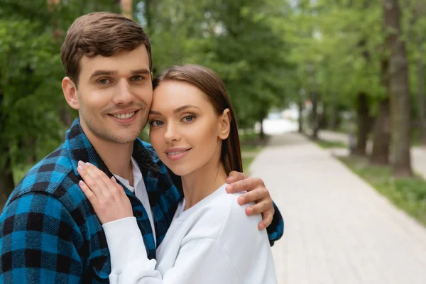 Handsome boyfriend and pretty girlfriend hugging and looking at camera in park — Stock Photo