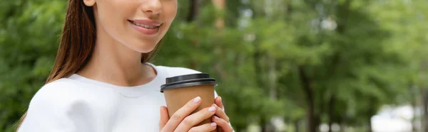 Récolte horizontale de fille heureuse tenant du café pour aller dans une tasse en papier — Photo de stock