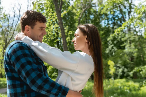 Vista lateral de pareja feliz y joven abrazándose en el parque - foto de stock