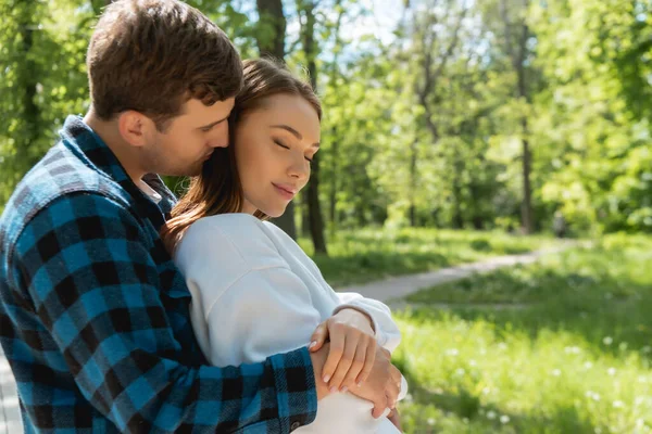 Felice studente abbracciare bella ragazza con gli occhi chiusi nel parco verde — Foto stock