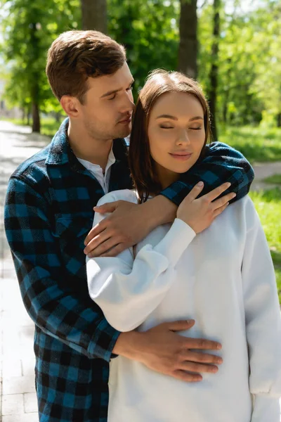 Happy student hugging beautiful girlfriend with closed eyes in green park — Stock Photo