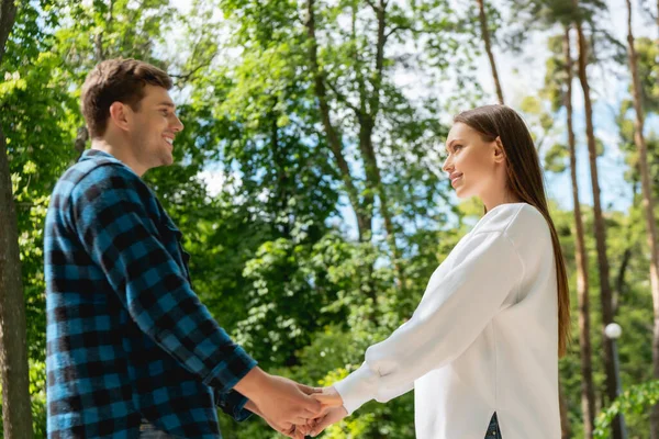 Profile of happy young couple holding hands in park — Stock Photo